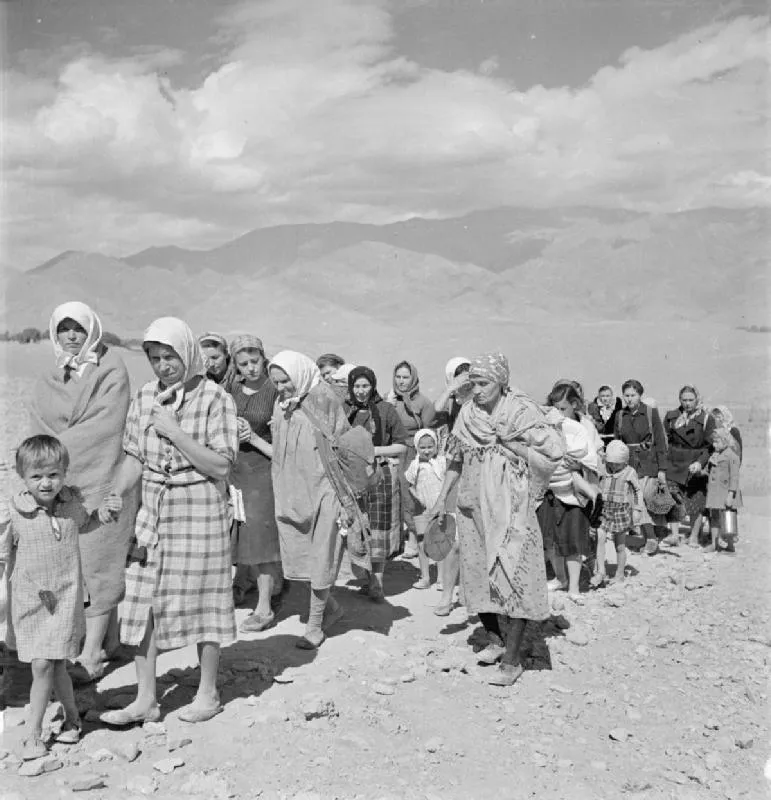 Black-and-white photograph of Polish refugees, mostly women and children, walking with bundles and suitcases over bare mountain ground on the route into Persia in 1942.